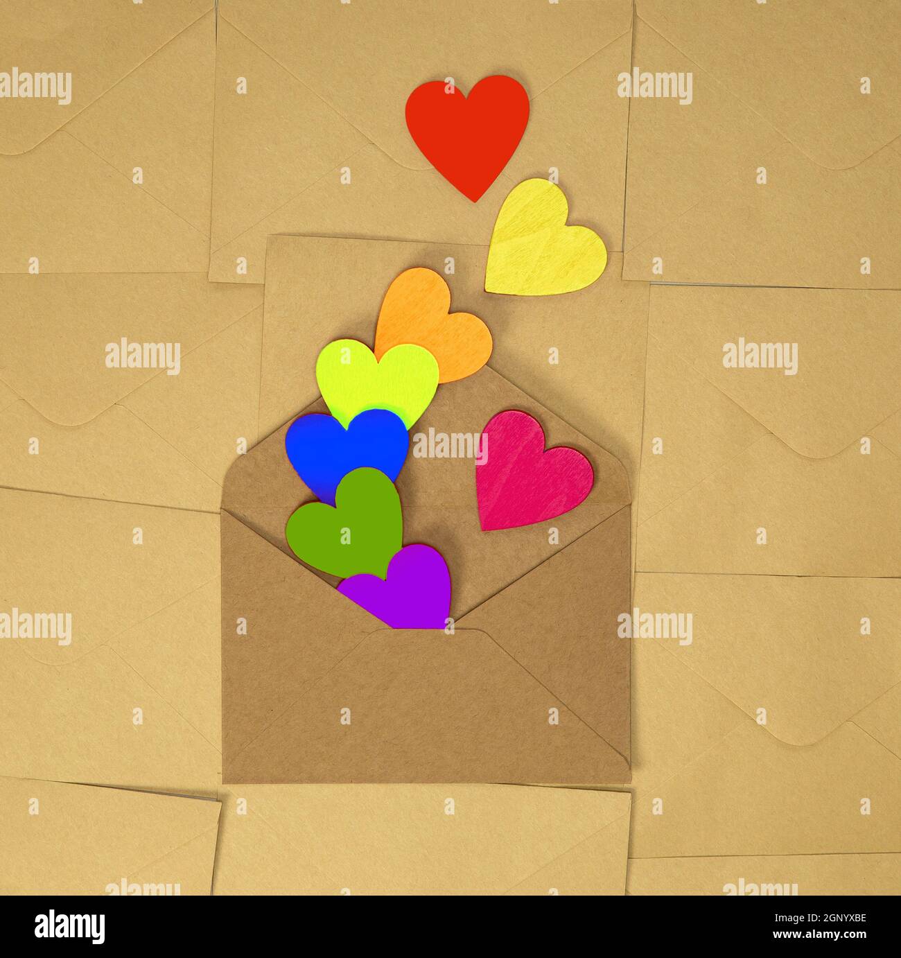 Brown craft paper envelope with various rainbow colorful hearts on plain brown background texture top view, Valentines Day, romantic concept copy spac Stock Photo