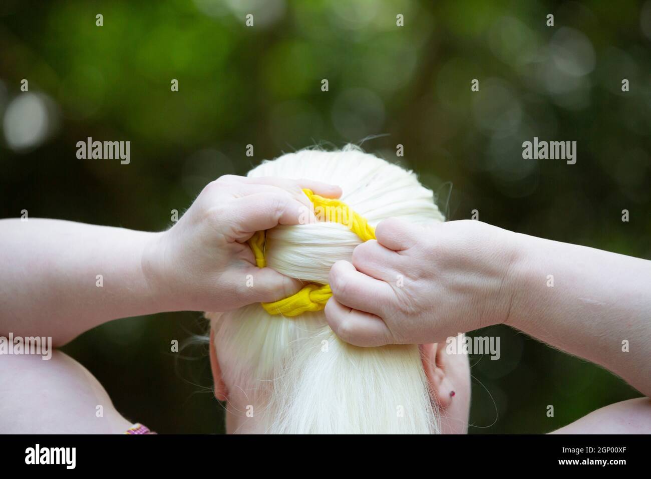 Woman wrapping her long, white hair into a yellow scrunchie Stock Photo
