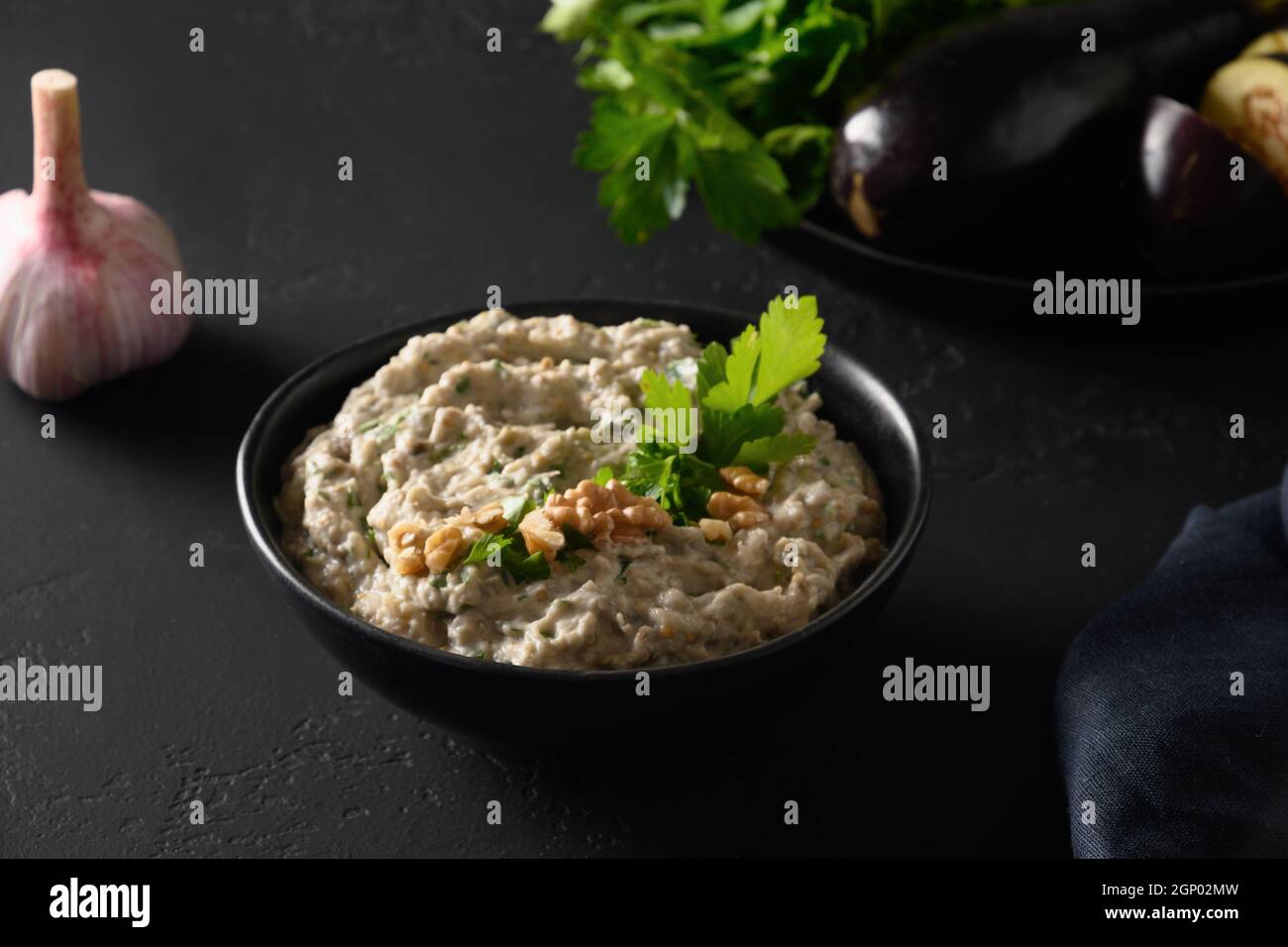 Baba ganoush Asian cuisine appetizer made from baked eggplant with parsley, garlic and olive oil on black table. Close up. Middle Eastern cuisine, veg Stock Photo