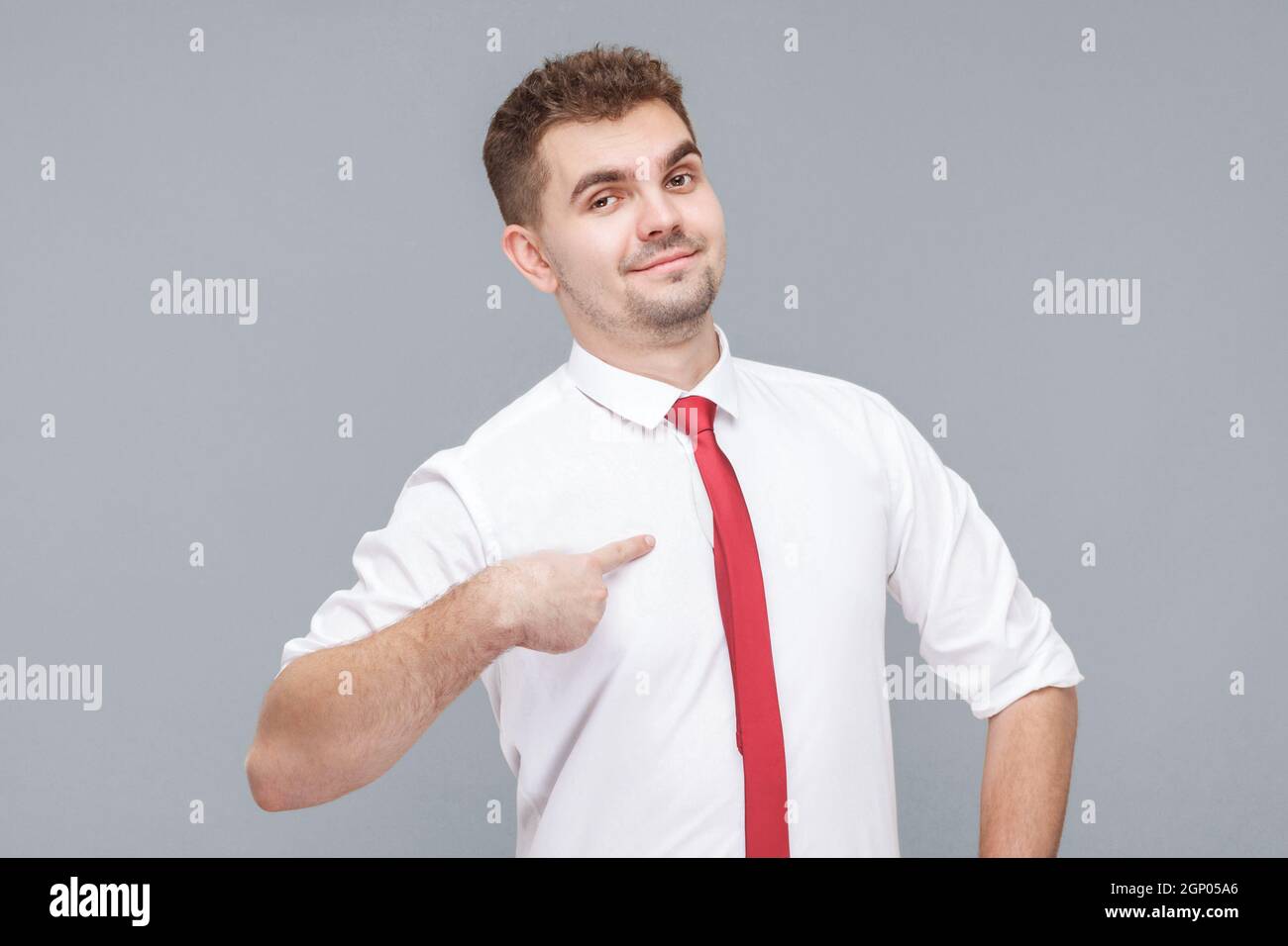 This is me. Portrait of young handsome proud man in white shirt and tie standing, pointing himself and looking at camera with proud face and confidence. indoor isolated on gray background. Stock Photo