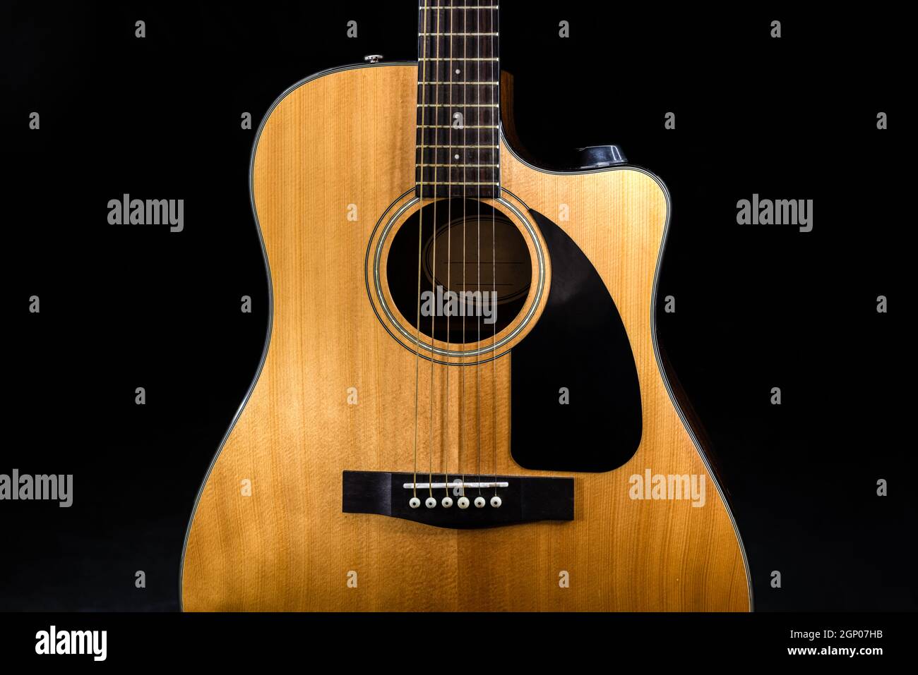 body of a classic acoustic six-string guitar with a yellow sound board and black pickguard on isolated black background Stock Photo