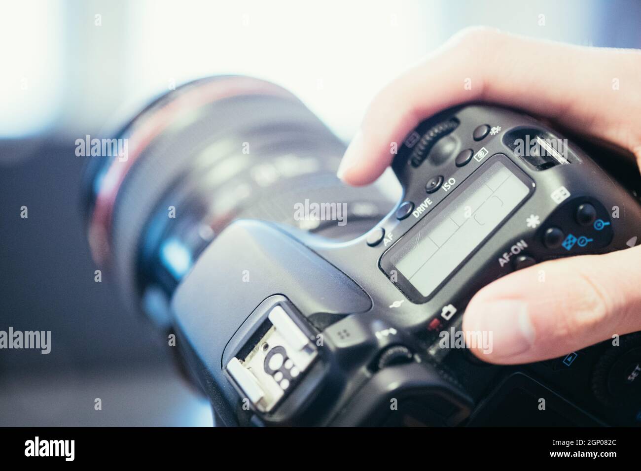 Photographer is holding a professional camera with telephoto lens in his hand, laptop in the blurry background Stock Photo