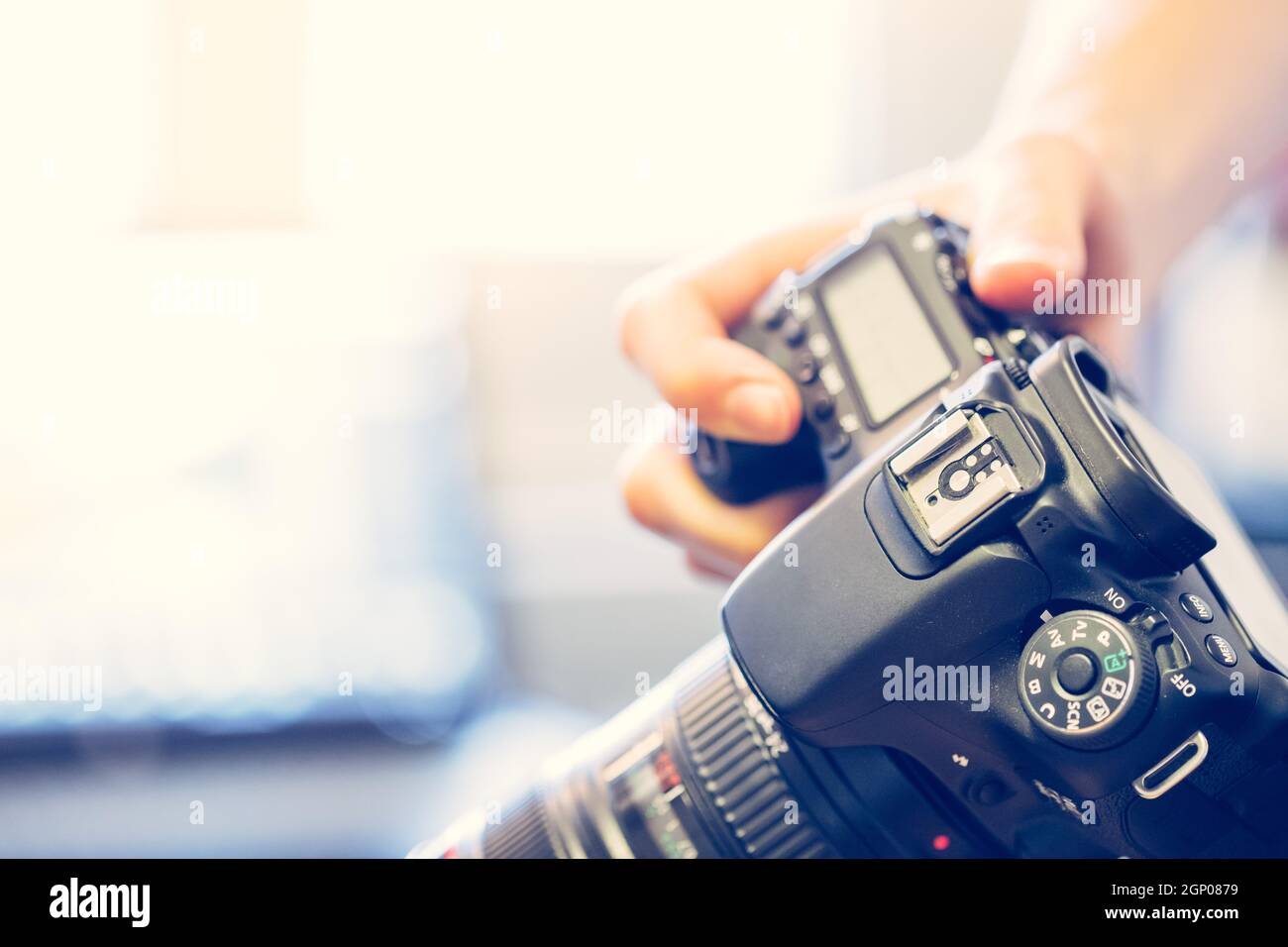 Photographer is holding a professional camera with telephoto lens in his hand, laptop in the blurry background Stock Photo