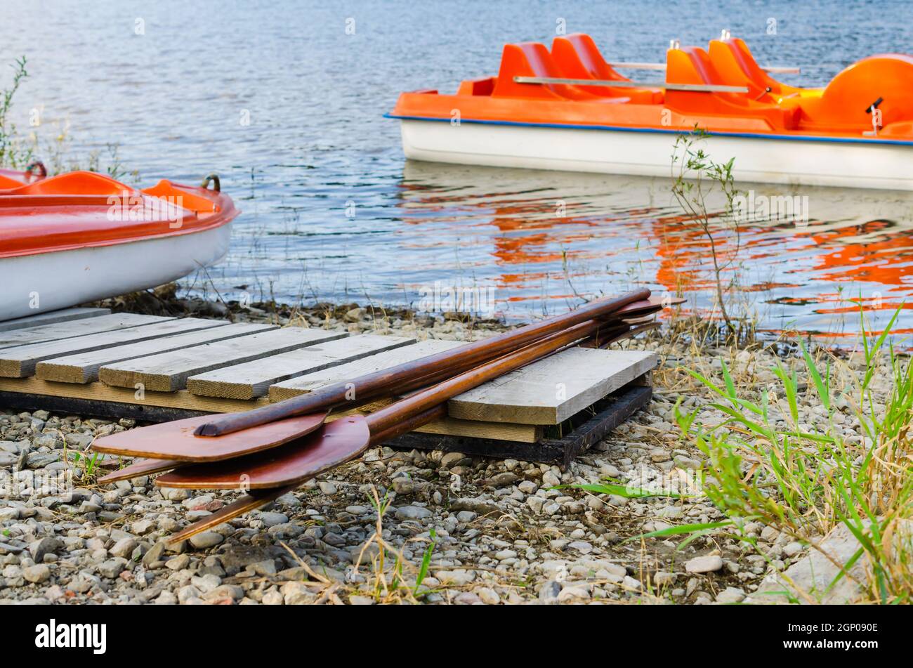 Wooden oars lie on the shore. Pleasure catamarans or boats on lake moored at the pier. Tourism in national park holiday. Active summer vacation. Stock Photo