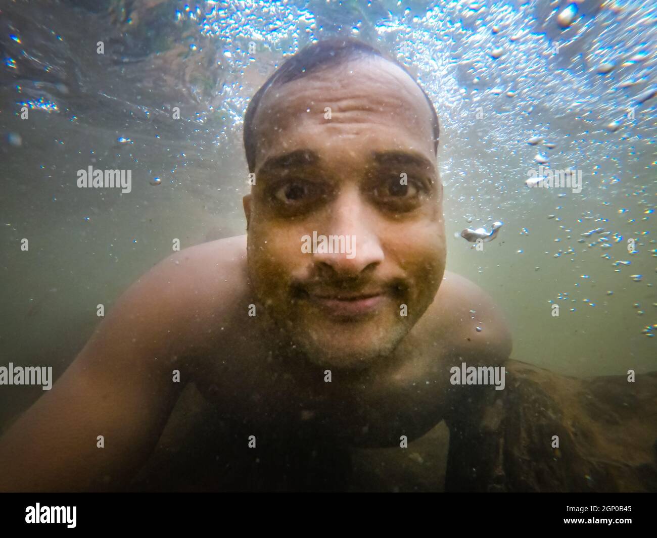 man swimming in natural waterfall underwater shot from low angle Stock