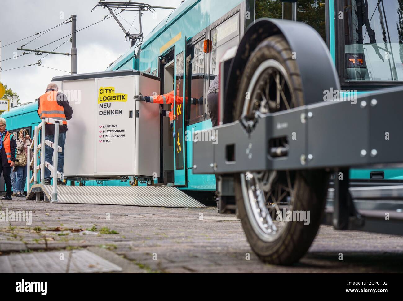 28 September 2021, Hessen, Frankfurt/Main: At the opening of the National Bike Logistics Conference, employees of VGF Verkehrsgesellschaft Frankfurt roll a container from a cargo bike manufacturer out of a tram to a waiting cargo bike (r) during a press demonstration. VGF plans to use the idea of a cargo tram initially for internal company transport. The conference will focus on the question of what sustainable, intermodal logistics chains can look like. Photo: Frank Rumpenhorst/dpa Stock Photo