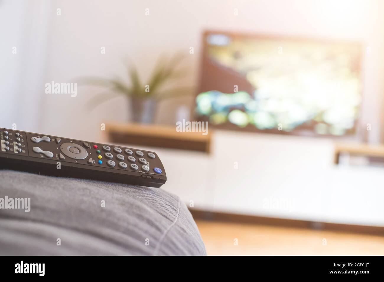 TV remote control in the foreground, tv in the blurry background. Streaming. Stock Photo