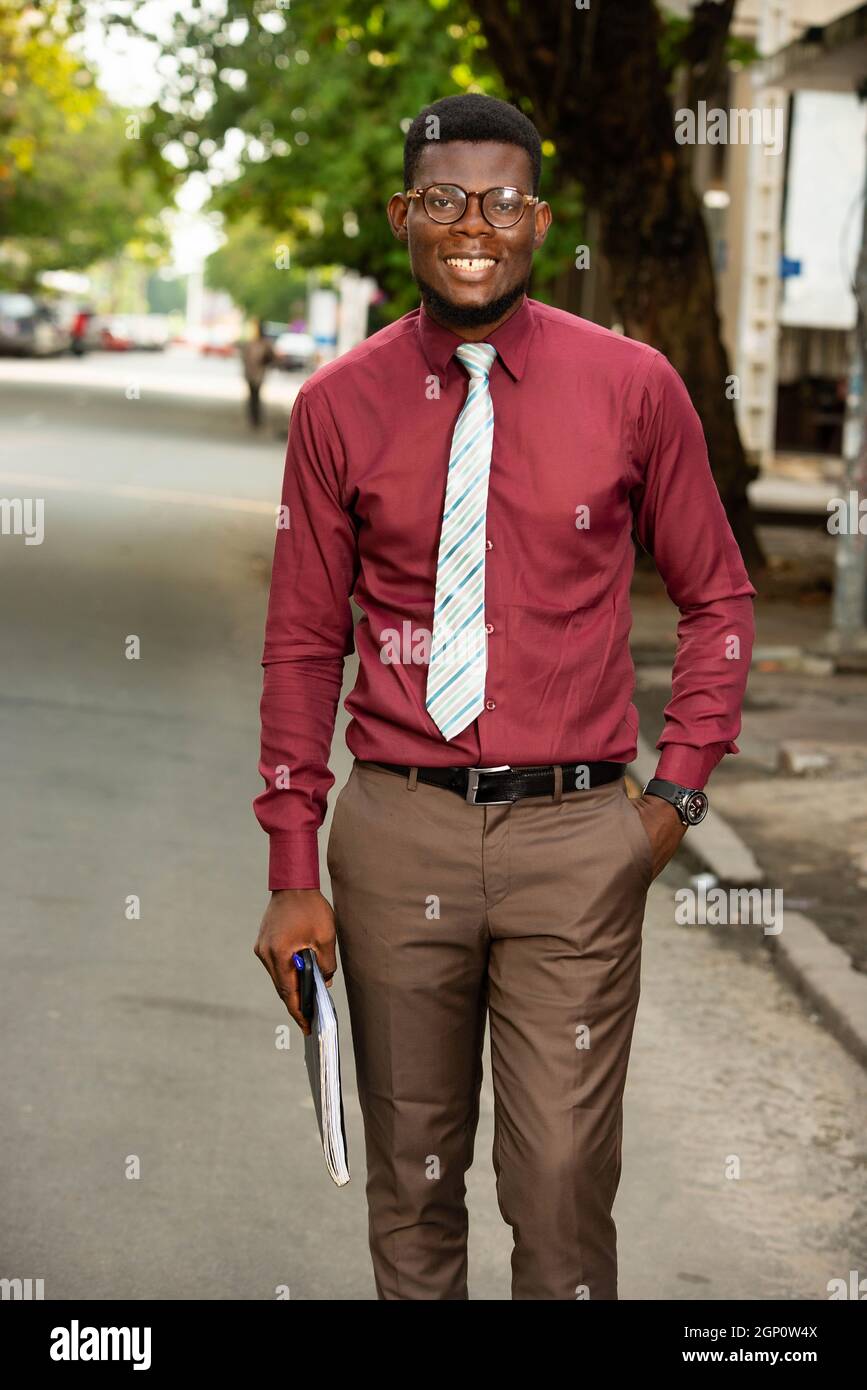 Photo of young beautiful african outdoor walking holding a notebook in his  arm clad in brown pants and a very elegant burgundy red chemise wearing gla  Stock Photo - Alamy