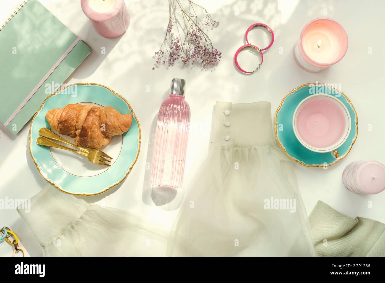 Female morning routine with  croissant, cup of pink flowers tea, earrings, flowers, blouse in sunrise  light on table . Top view Stock Photo