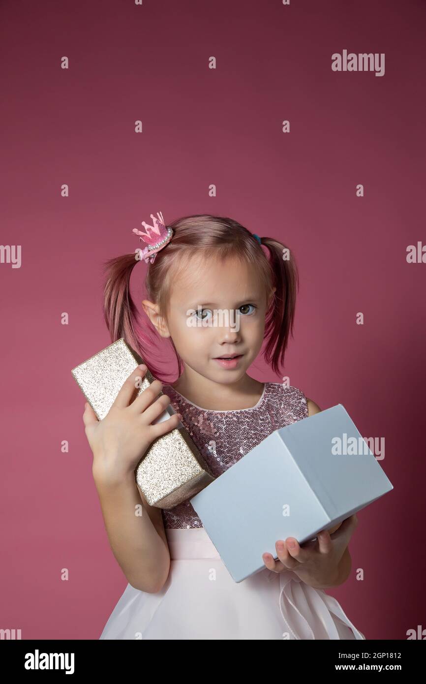 Little caucasian girl in a festive dress with sequins posing opening gift box Stock Photo