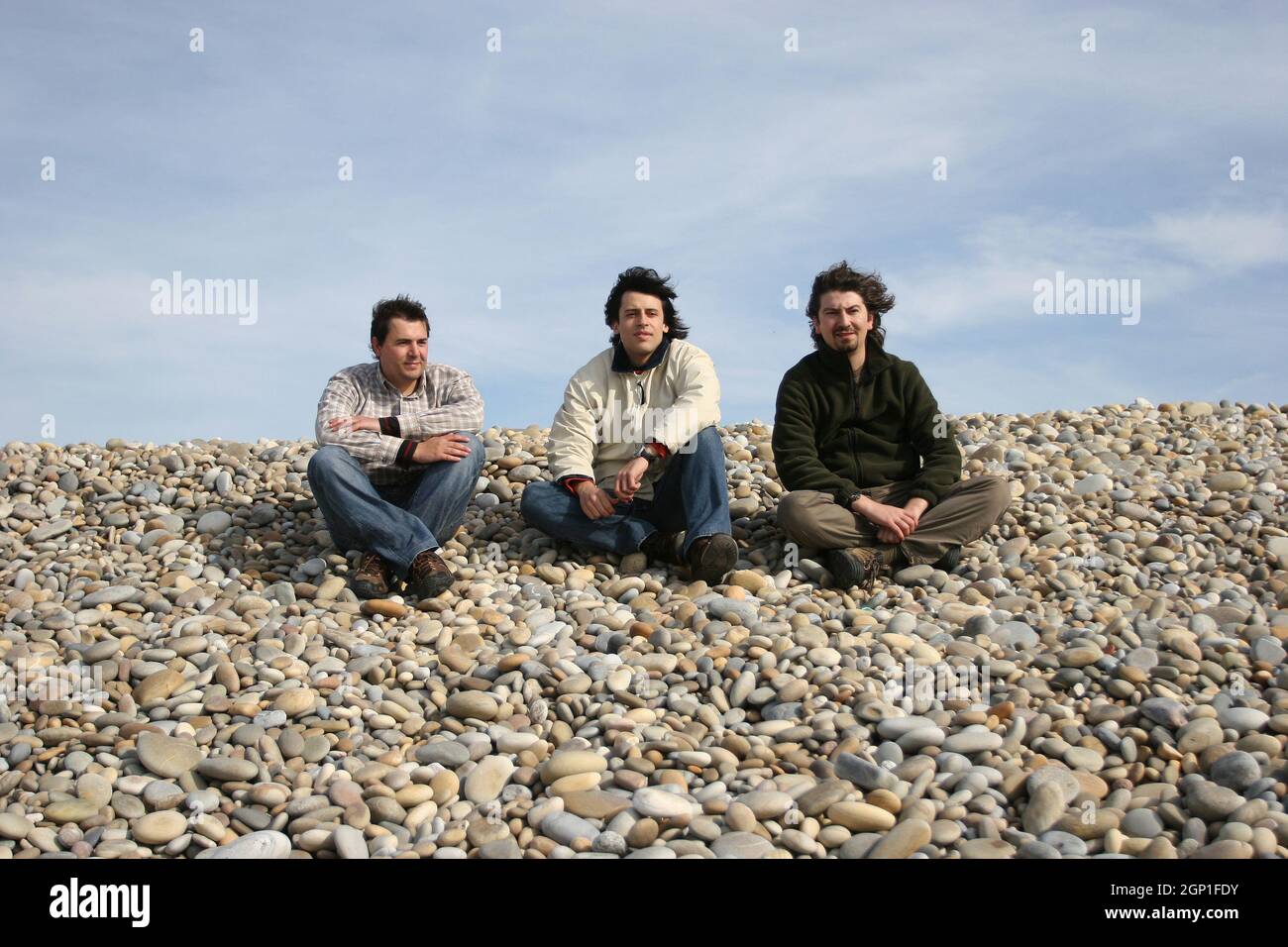 three casual young men at the beach, isolated in blue sky background Stock Photo