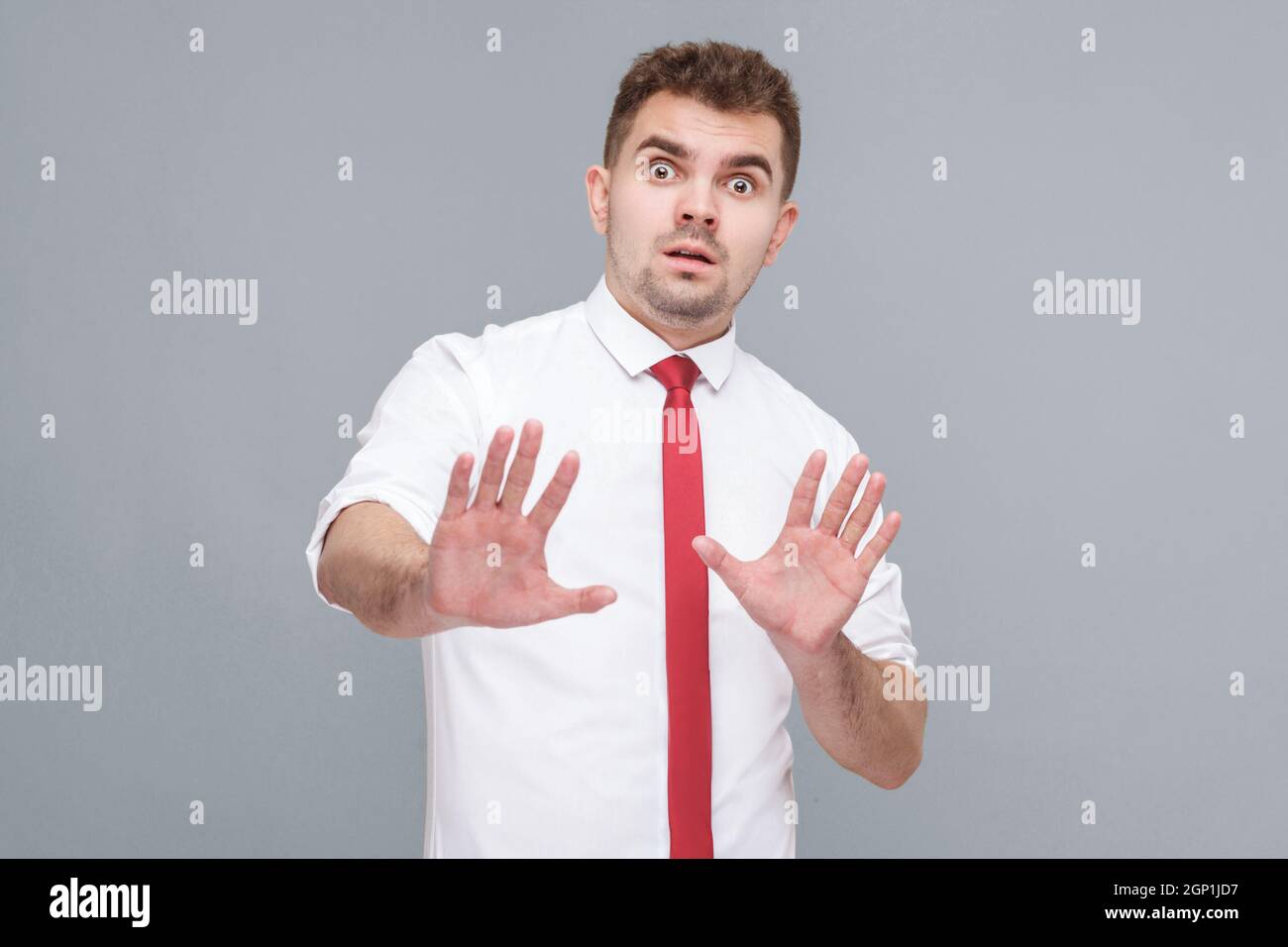 no, stop. Portrait of young scared man in white shirt and tie standing and looking at camera with afraid face and showing stop with hands. indoor isolated on gray background. Stock Photo