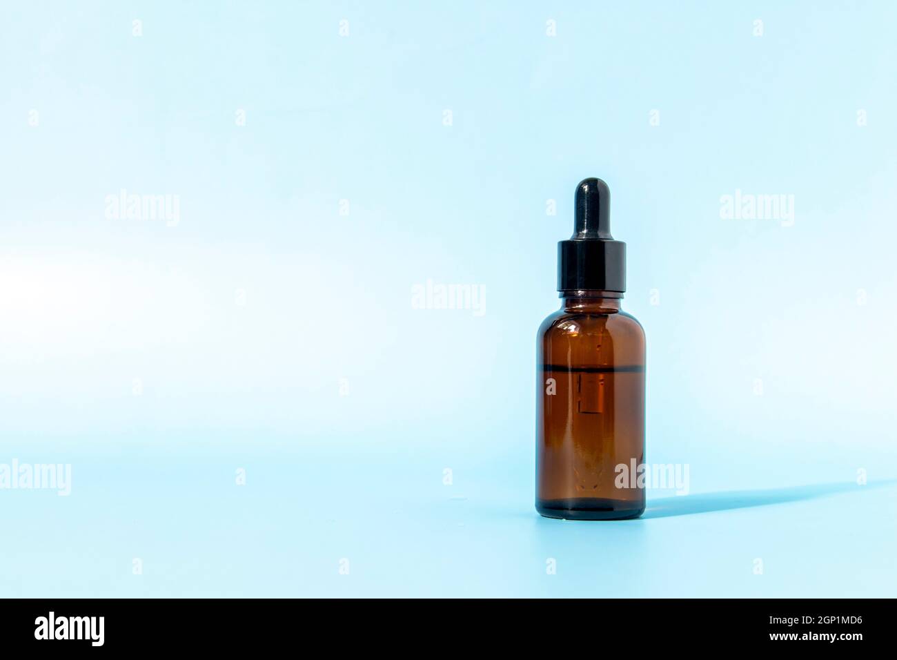 Glass dropper bottle made of brown glass on a blue background casts a shadow. Front view with copy space. Mockup of a cosmetic product. Serum for skin Stock Photo