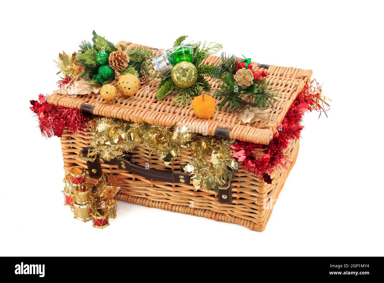 Closed Wicker basket overflowing with red and gold tinsel isolated with Christmas decorations resting on the lid isolated on white background Stock Photo