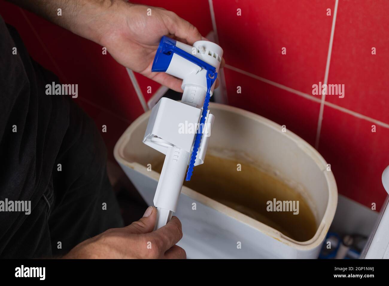 Toilet tank parts replacement. A man in orange gloves repairs the toilet tank drain Stock Photo