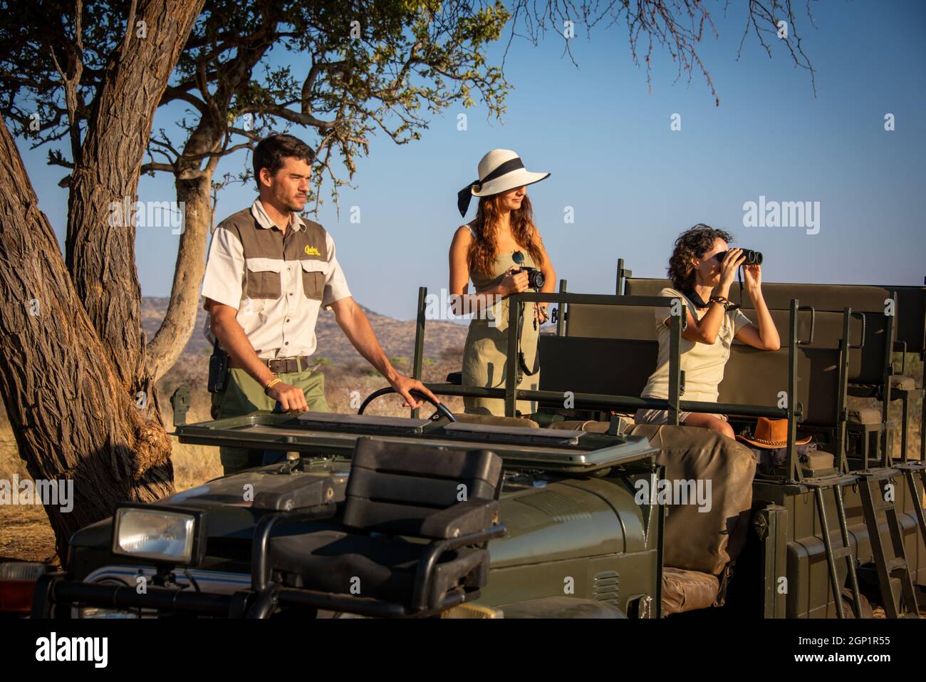Guide and guests in jeep by tree Stock Photo