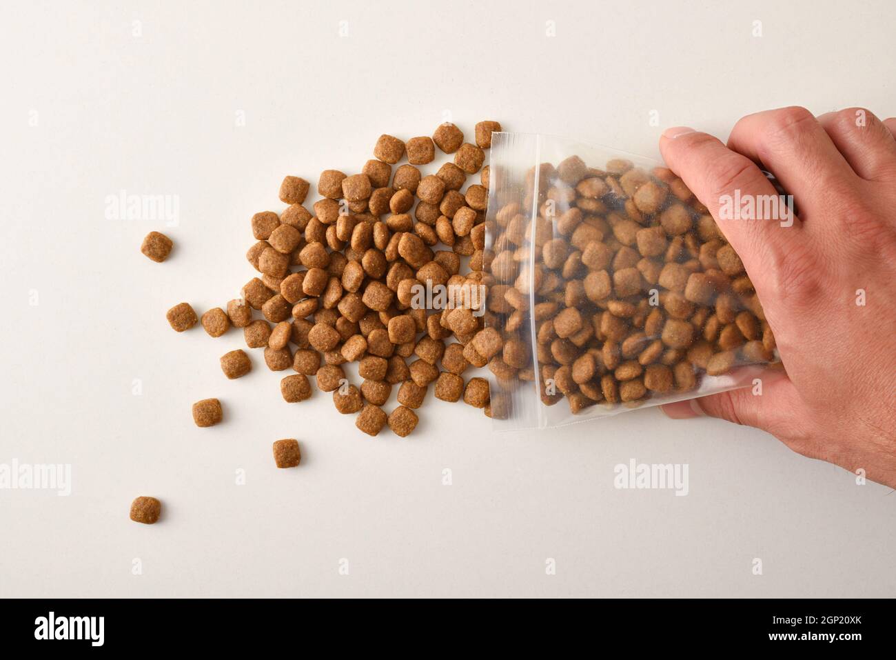 Man's hand dropping dog kibble from a clear plastic bag onto a white table. Top view. Horizontal