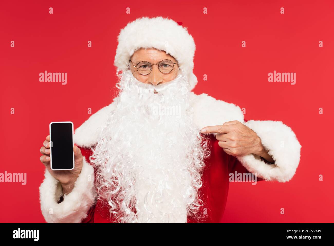 Santa claus pointing at smartphone with blank screen isolated on red ...