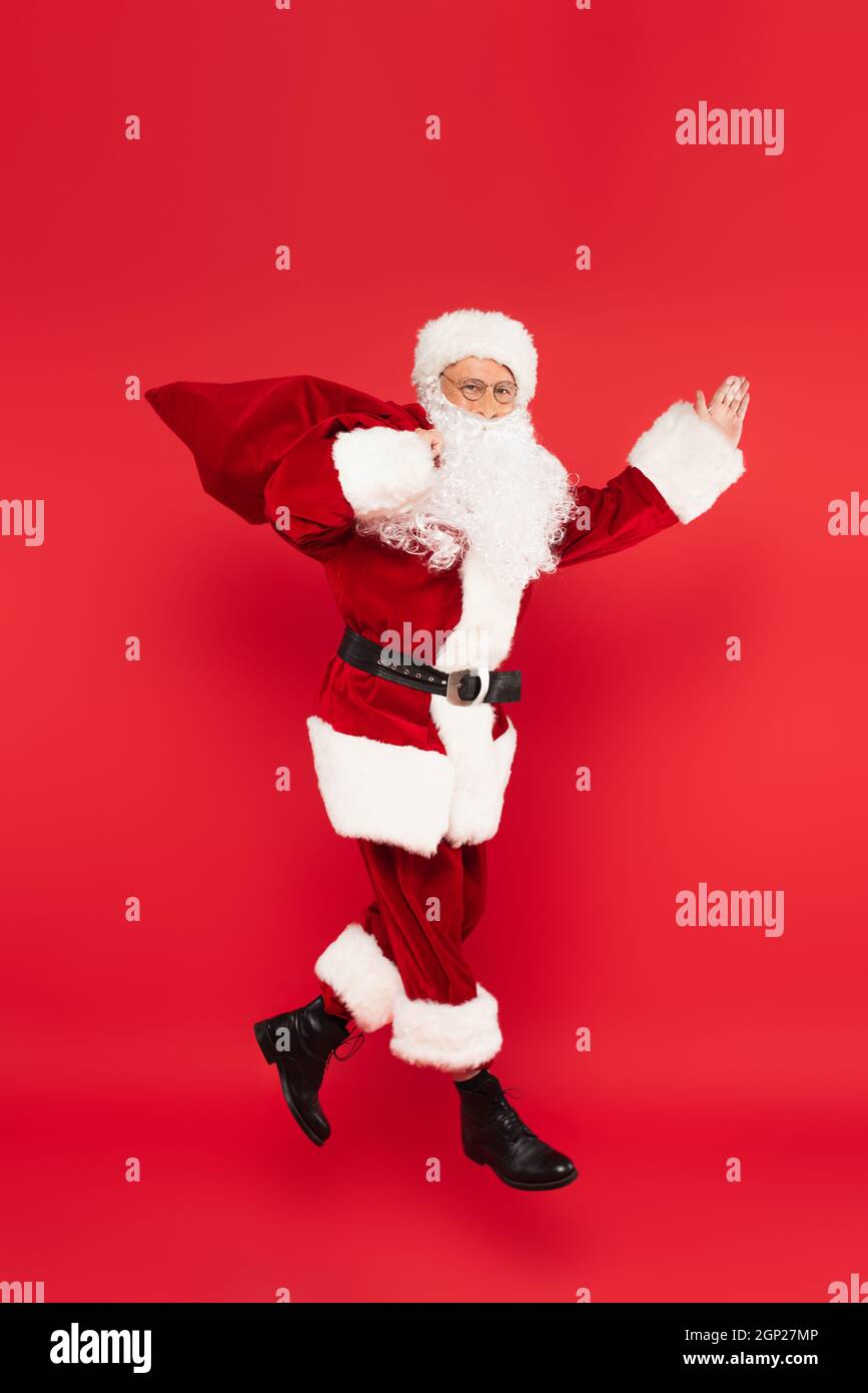 Santa claus with sack pointing with hand and levitating isolated on red ...