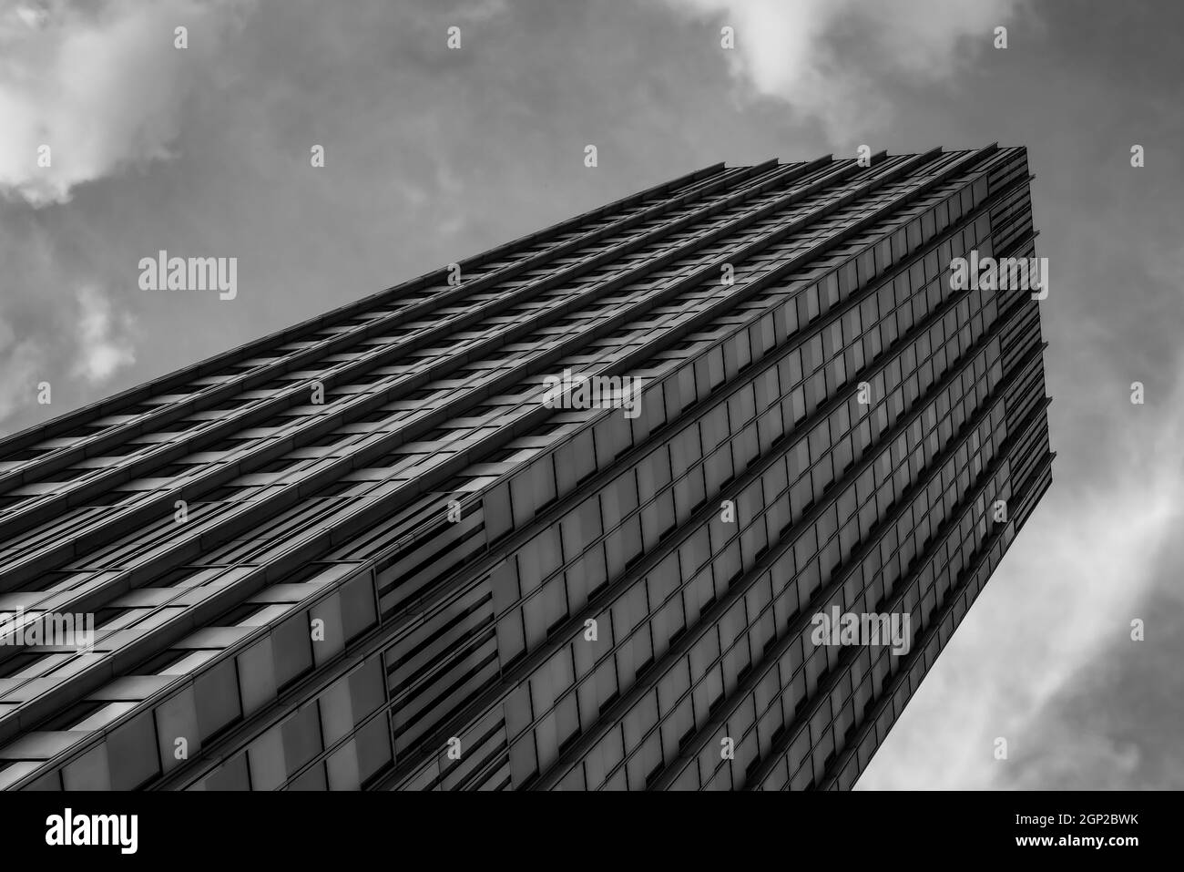 Grayscale low angle shot of a tall skyscraper with a cloudy sky above ...