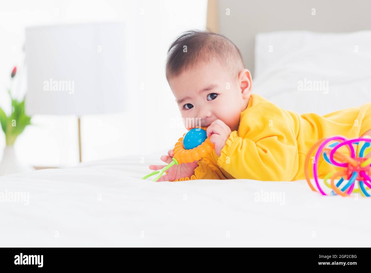 Portrait of beautiful young Asian newborn little baby prone on the bed at home, Happy baby smile wears a yellow shirt relaxing in the room, Family mor Stock Photo