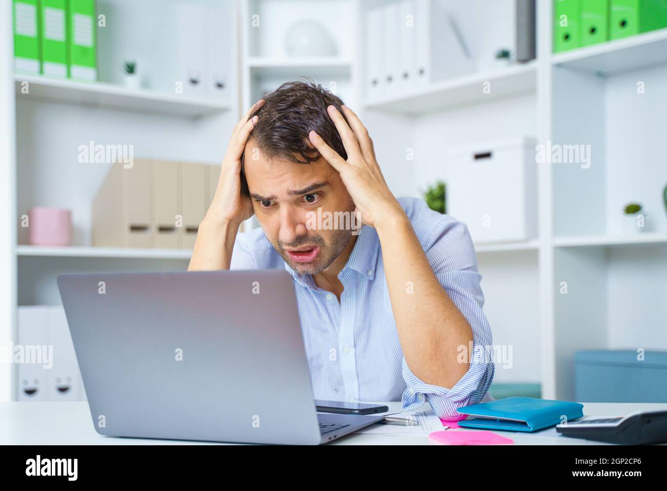 Businessman sitting at work desk with laptop, feeling exhausted with financial problem Stock Photo