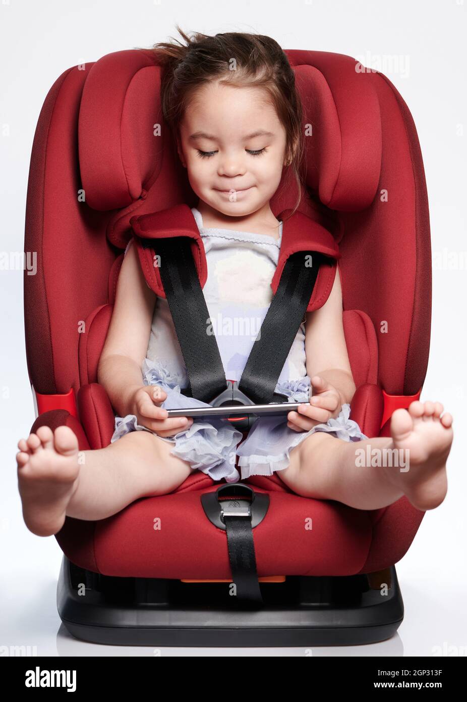 Happy girl kid in car chair with smartphone isolated on studio
