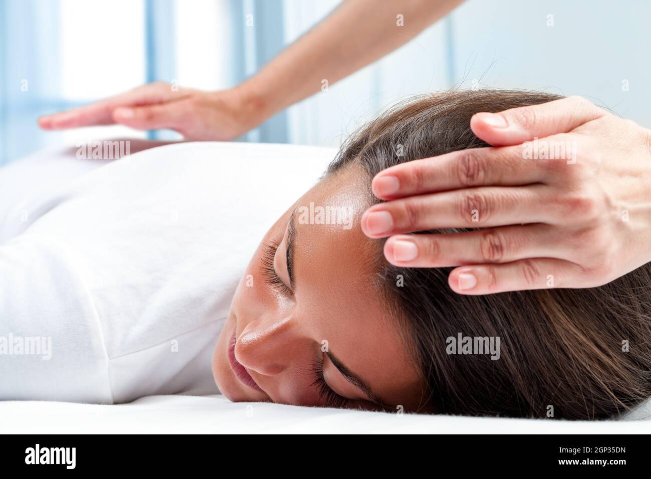 Therapists hands doing reiki therapy on girl. One hand on head and one hand on back. Stock Photo