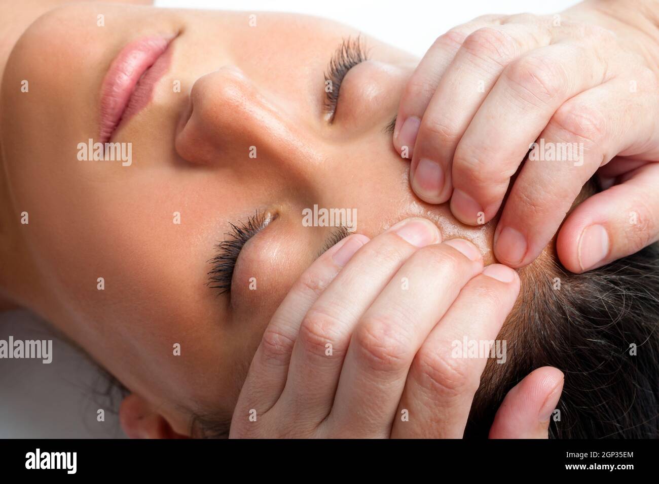 Macro close up face shot of young woman receiving massage. Therapist hand doing manipulative treatment on forehead. Stock Photo