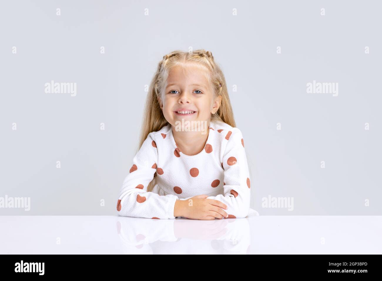 Portrait of little preschool girl, child calmly sitting isolated over white studio background