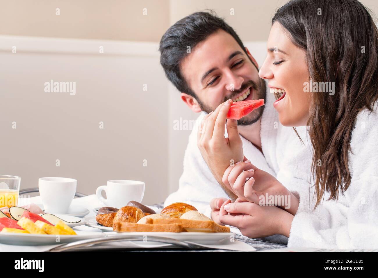 Close up fun portrait of couple in bathrobe on bed enjoying breakfast ...