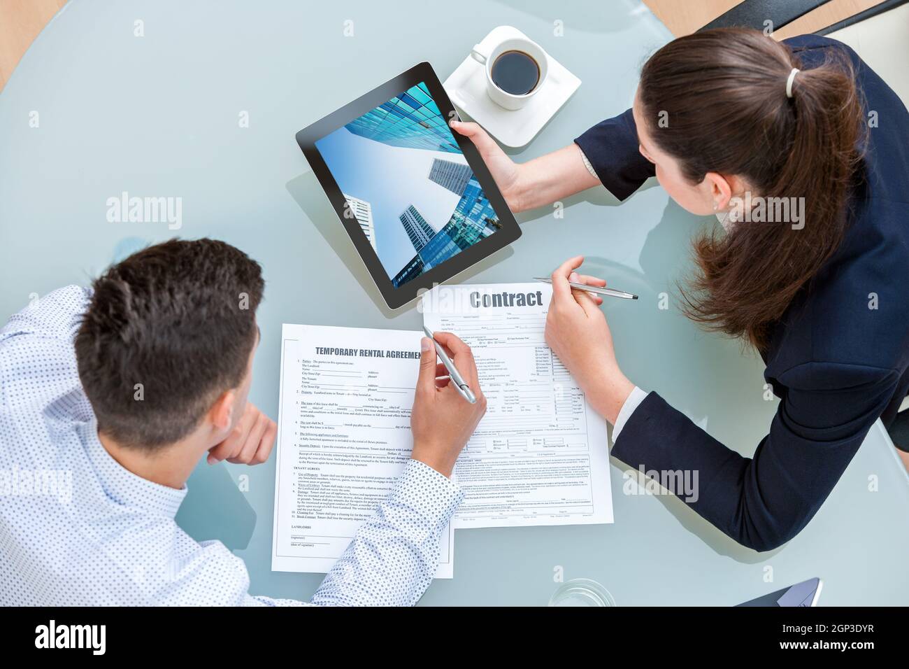 Young business couple discussing rental agreement. Woman showing man office buildings on digital tablet at table. Stock Photo