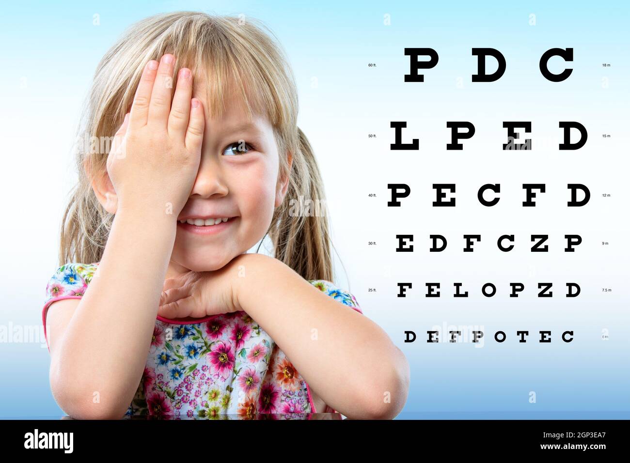 Close up portrait of cute little infant reviewing eyesight on chart. Girl closing one eye with hand reading vision chart. Stock Photo