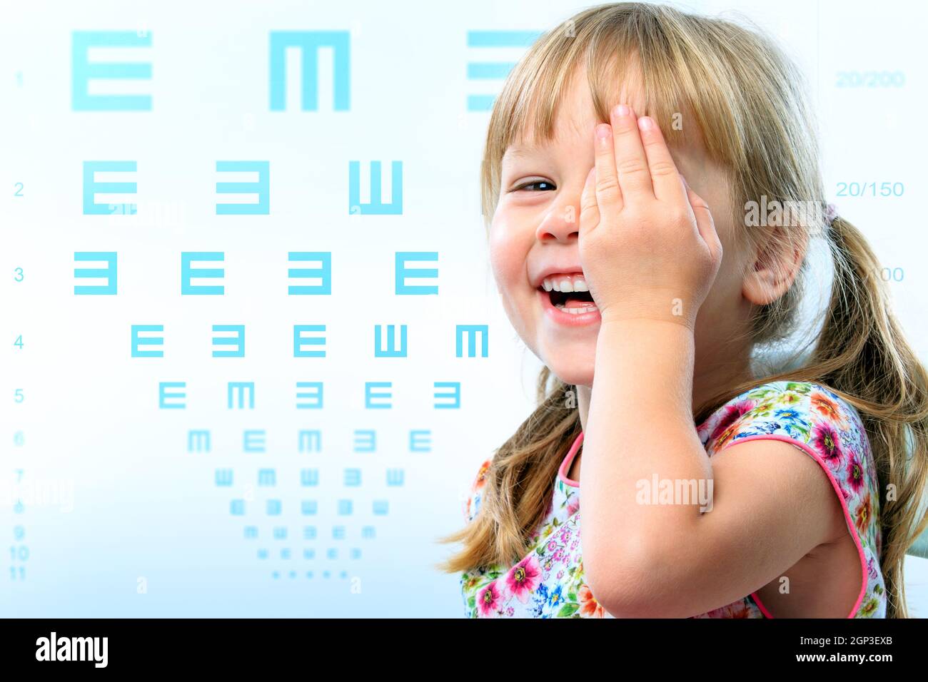 Close up fun portrait of little girl testing eye sight.Vision test chart in background. Stock Photo