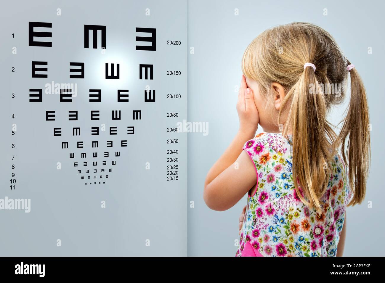 Close up rear view of little girl looking at eye test chart.Kid closing one eye with hand. Stock Photo