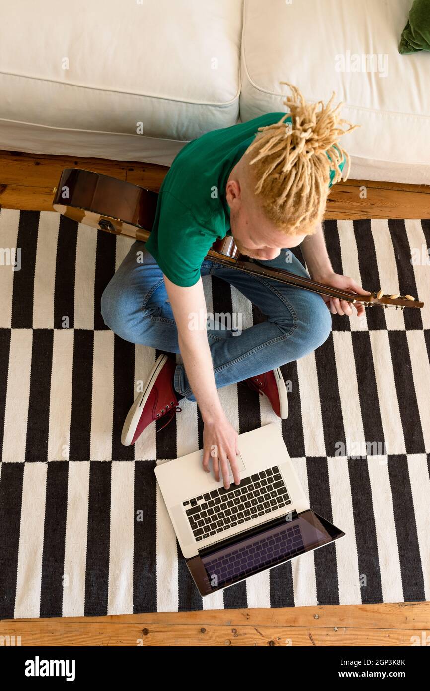 Albino african american man in the living room playing guitar and using laptop Stock Photo