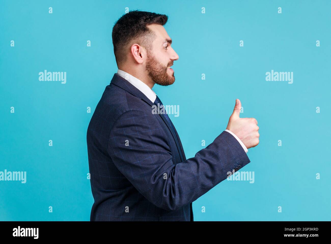 https://c8.alamy.com/comp/2GP3KRD/well-done-good-job!-profile-portrait-of-smiling-happy-bearded-man-wearing-dark-official-style-suit-looking-ahead-showing-thumb-up-indoor-studio-shot-isolated-on-blue-background-2GP3KRD.jpg