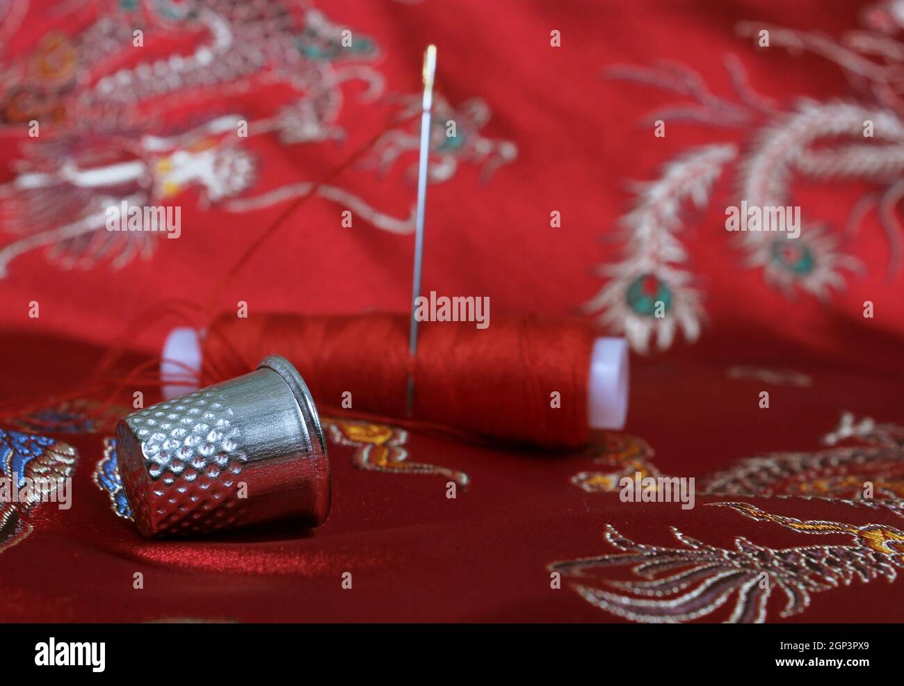 Thimble and Thread on Asian Red Silk Fabric Stock Photo