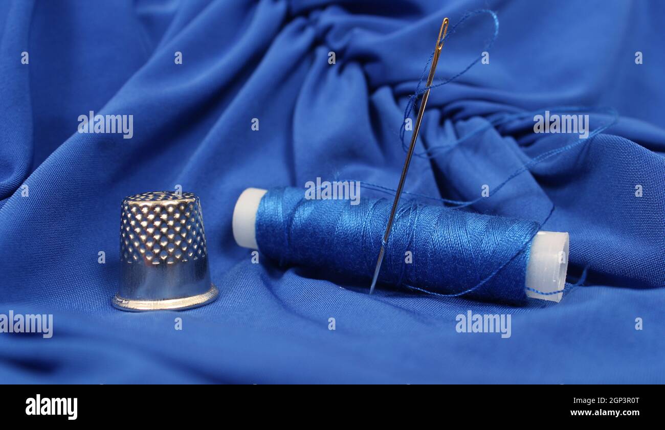 Thimble and Blue Thread on Blue Fabric Stock Photo