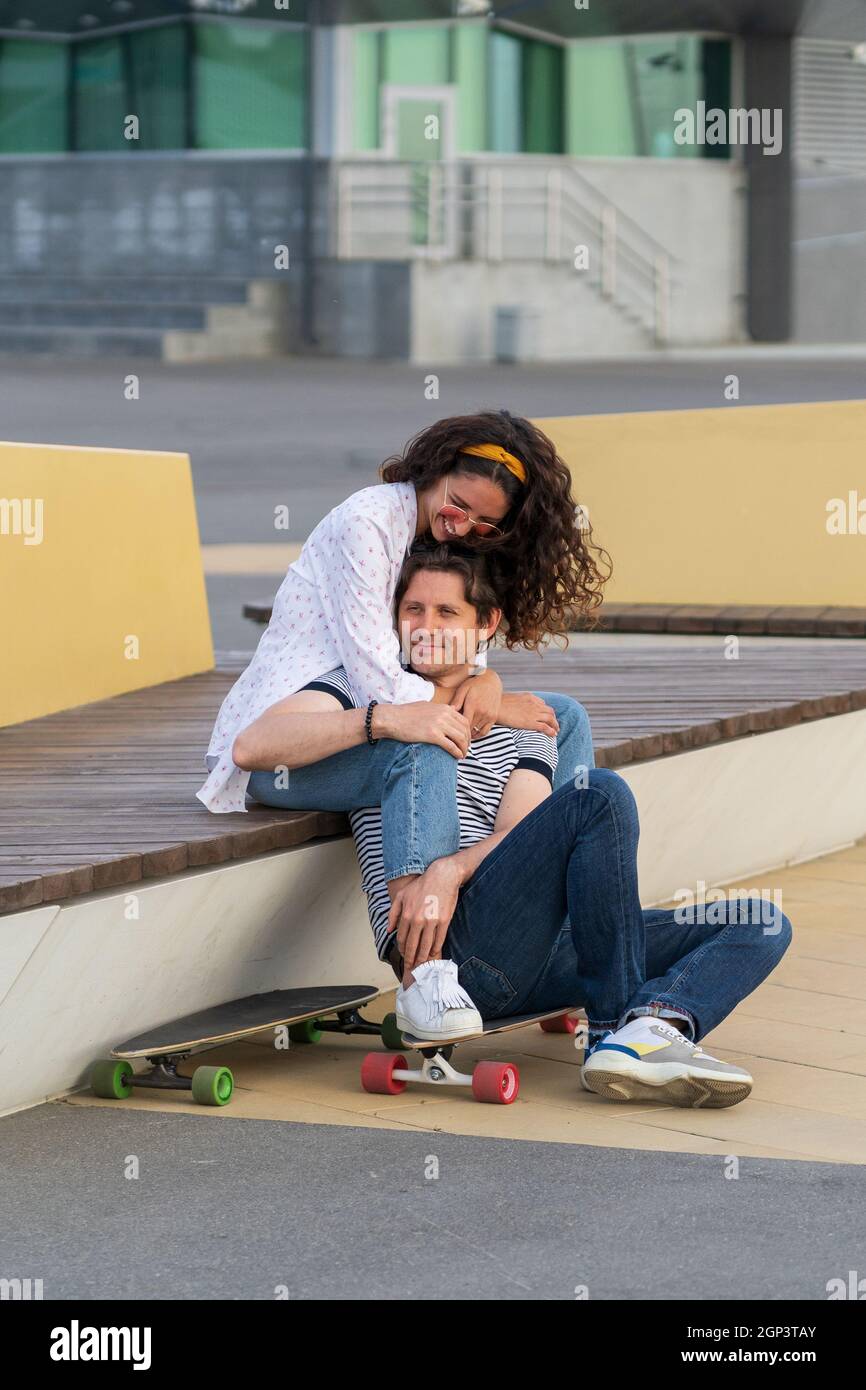 Young couple in love enjoy sunset sit hugging on longboard. Trendy man and woman chilling outdoor Stock Photo