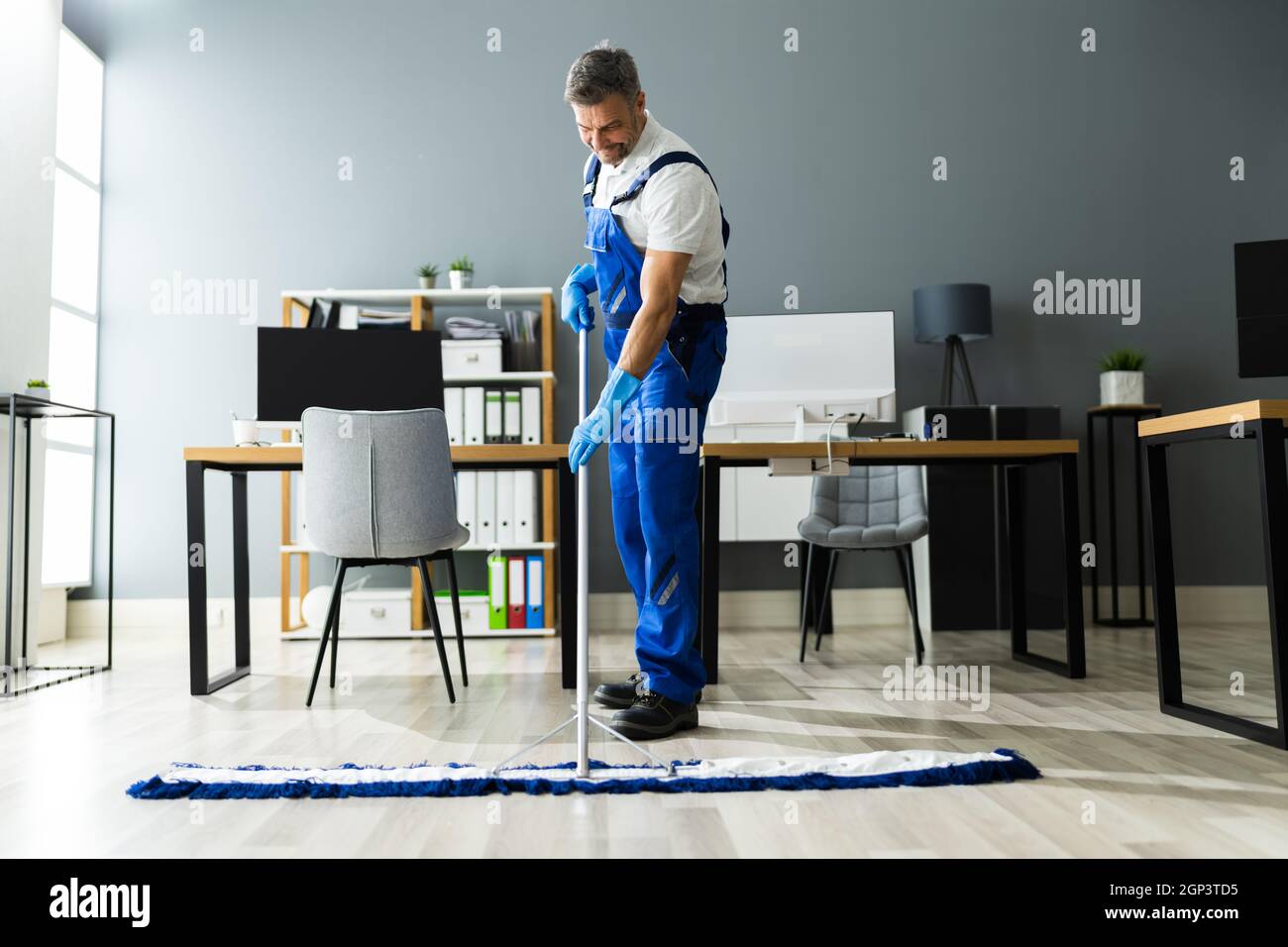 Male Janitor Mopping Floor In Face Mask In Office Stock Photo