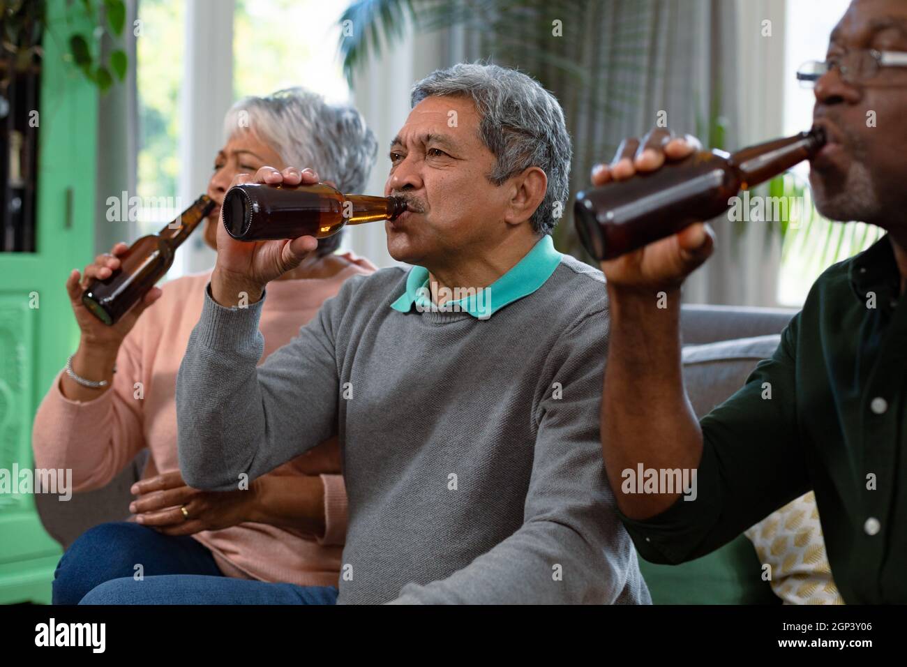 Two diverse senior couple and their african american male friend watching tv and drinking beer Stock Photo