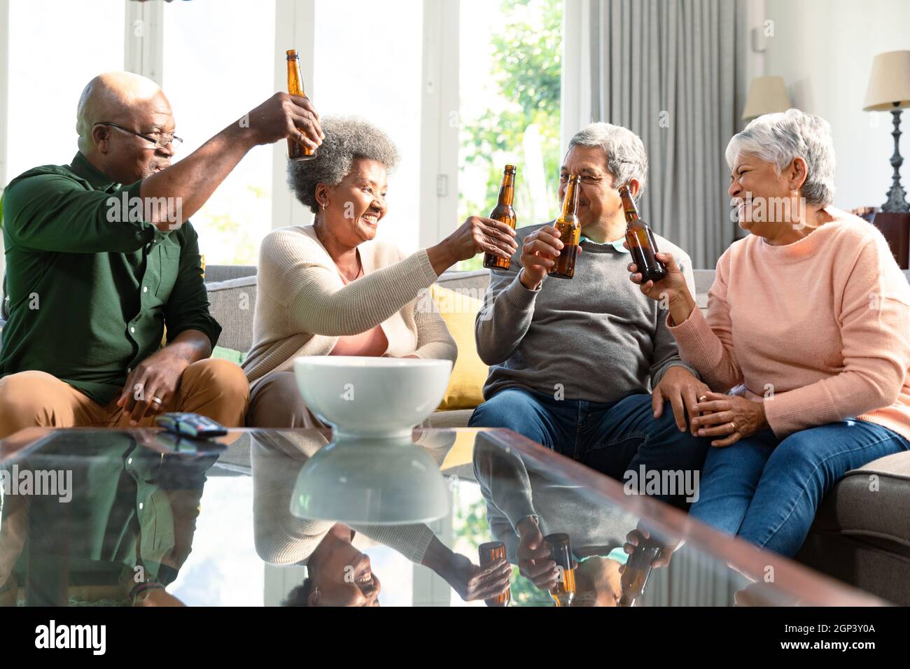 Two diverse senior couples sitting on sofa with beer and having fun Stock Photo