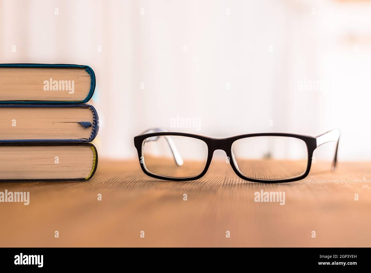 Stack of books and glasses lying on wooden desk at home. Knowledge and science Stock Photo