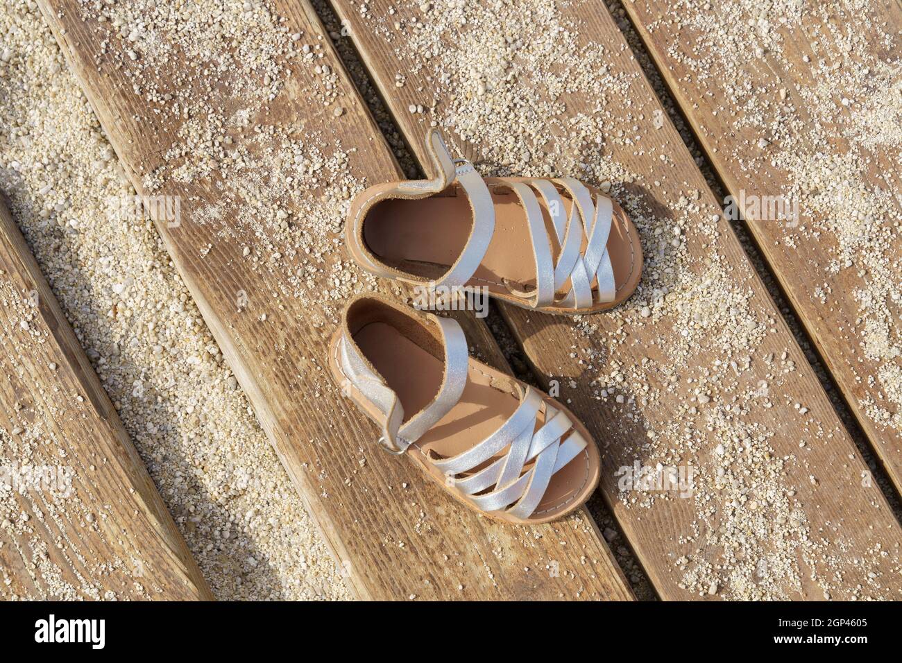 Kids silver leather sandals on wooden board with sand in sunny day Stock  Photo - Alamy