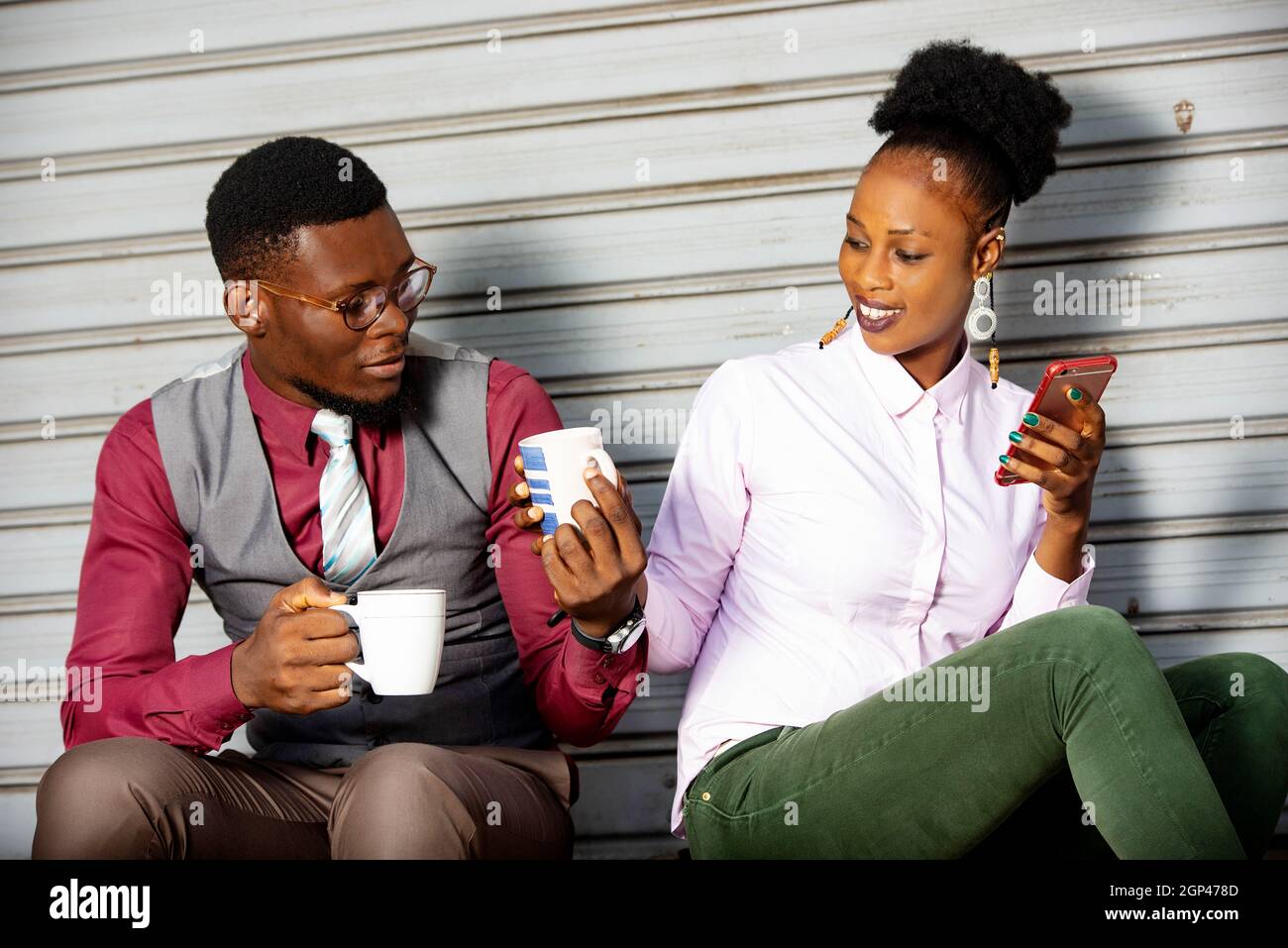 Young business people sitting outside sharing coffee during break while smiling. Stock Photo