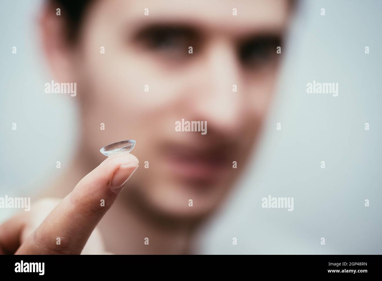Close up picture of contact lens on a mans finger. Face in the blurry