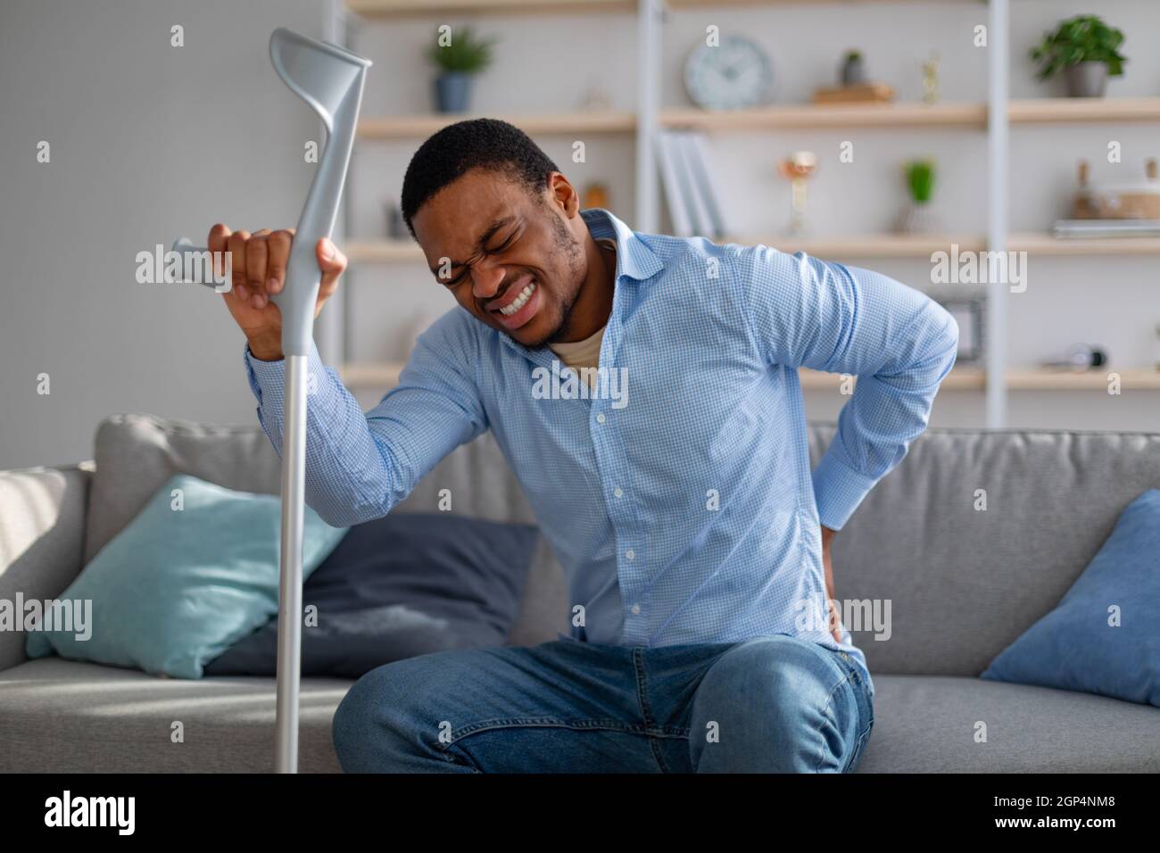 Young African American guy suffering from back pain, leaning on crutch