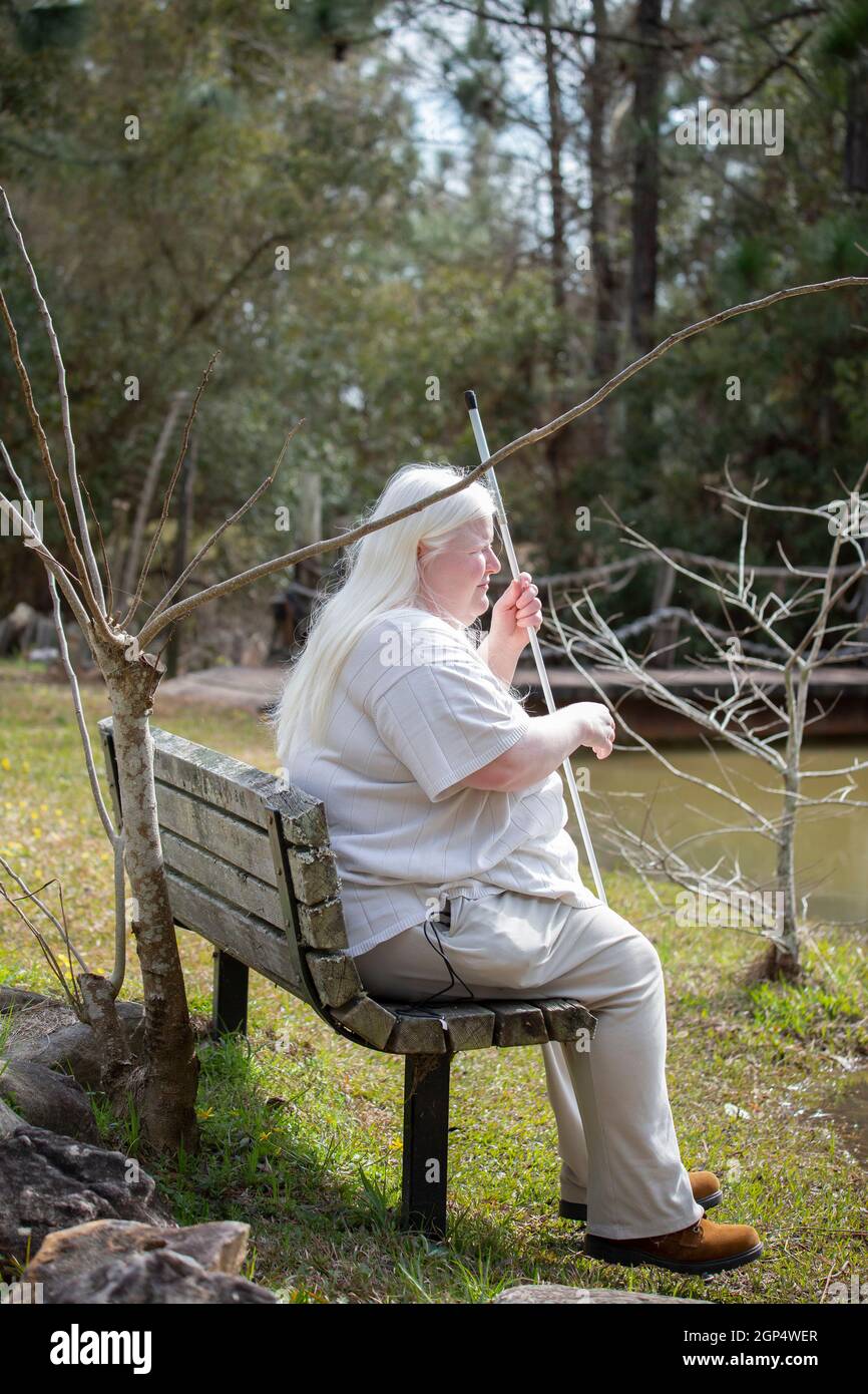 Blind woman sitting on a bench near a pond Stock Photo