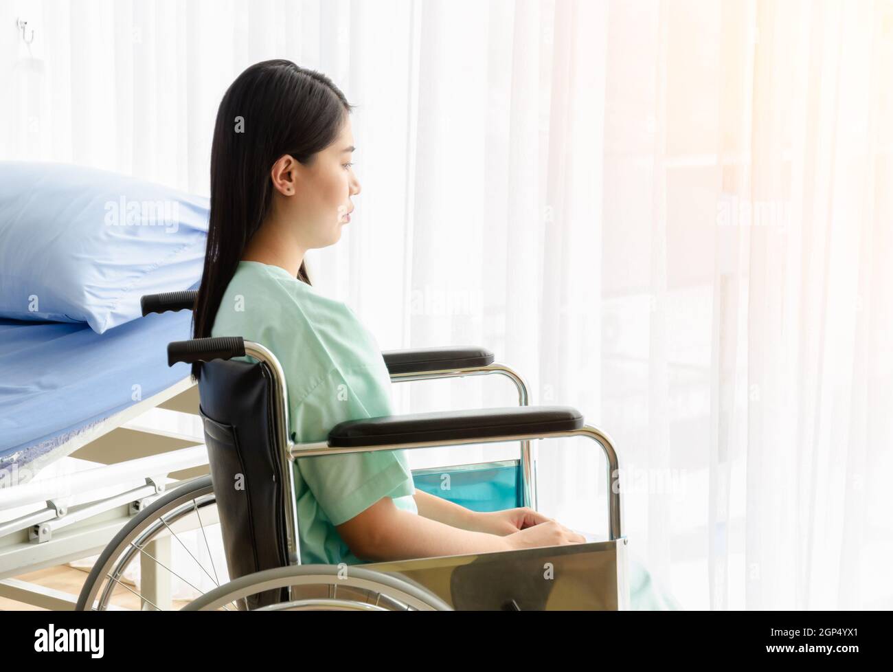 Patient sitting on wheelchair alone at hospital room looking through window. Sad woman feel depressed and lonely, healthcare and disability concept. Stock Photo